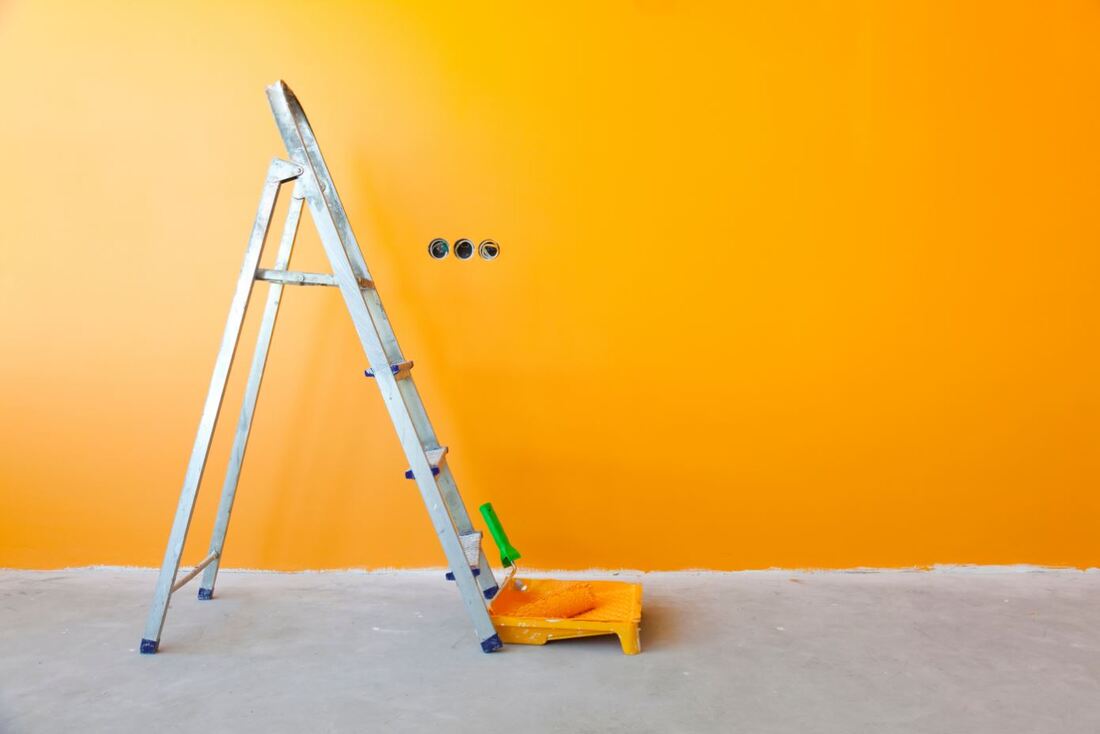 Yellow Painted wall with a ladder and roller in a paint tray in front of it