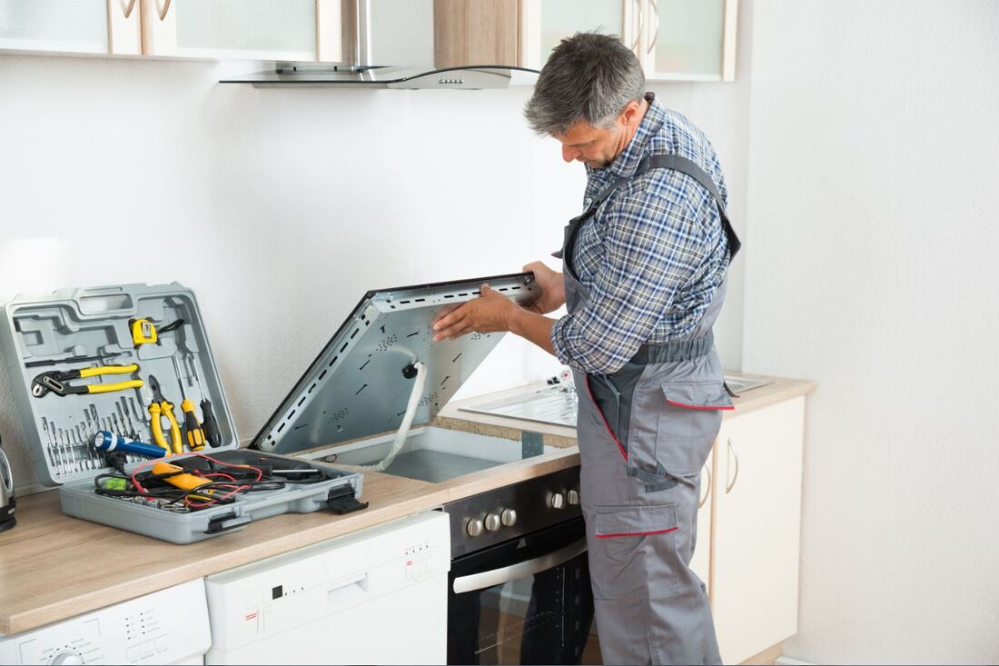 A repairman examining a stove in the kitchen
